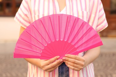 Woman with pink hand fan outdoors, closeup
