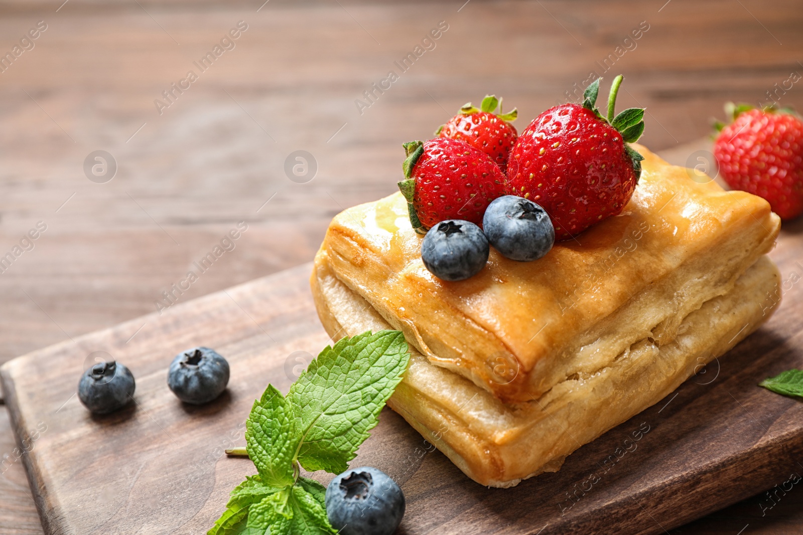 Photo of Fresh delicious puff pastry with sweet berries on wooden table, closeup. Space for text