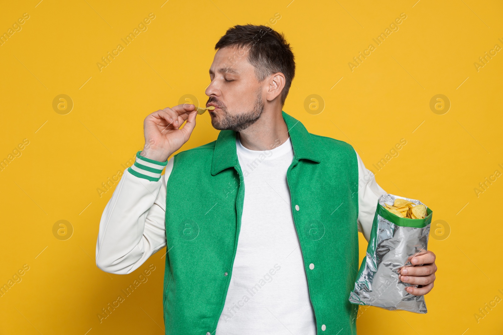 Photo of Handsome man eating potato chips on orange background