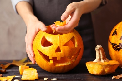 Photo of Woman making Halloween pumpkin head jack lantern on wooden table, closeup