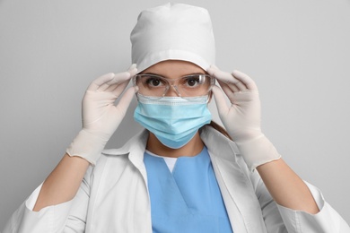 Photo of Doctor in protective mask and medical gloves putting on glasses against light grey background