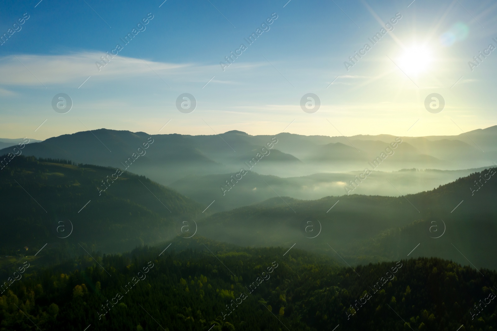 Image of Sun shining over forest in misty mountains. Drone photography