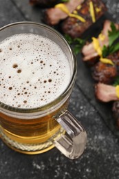 Photo of Mug with beer and delicious grilled ribs on dark grey textured table