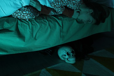 Photo of Childhood phobia. Girl looking at skull under bed indoors