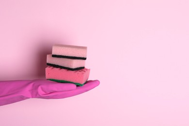 Photo of Woman in rubber glove holding sponges on pink background, closeup. Space for text