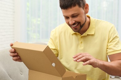 Happy man opening parcel on sofa at home. Internet shopping