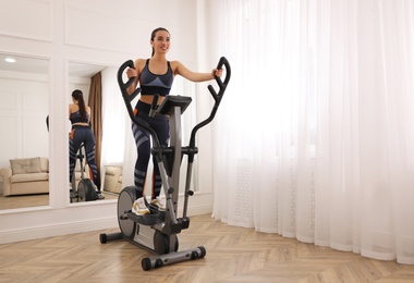 Woman using modern elliptical machine at home