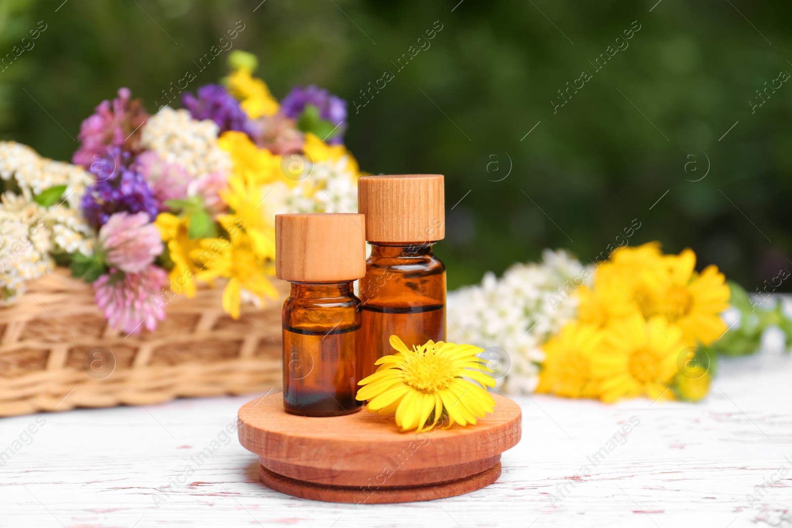 Photo of Bottles of essential oils and beautiful flowers on white wooden table