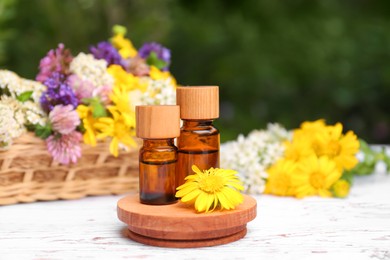 Photo of Bottles of essential oils and beautiful flowers on white wooden table