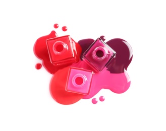 Spilled different nail polishes with bottles on white background, top view