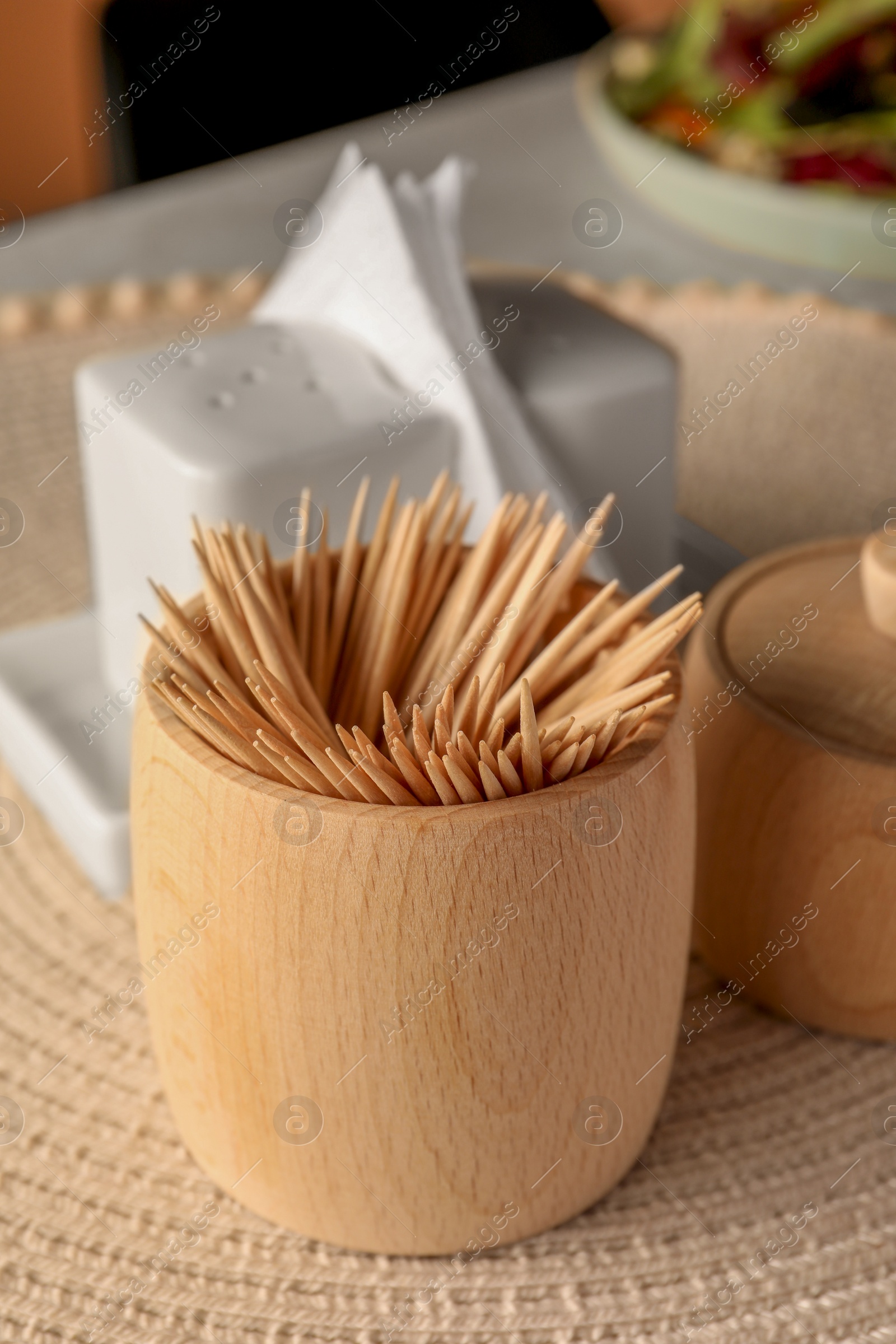 Photo of Wooden holder with many toothpicks on wicker mat, closeup