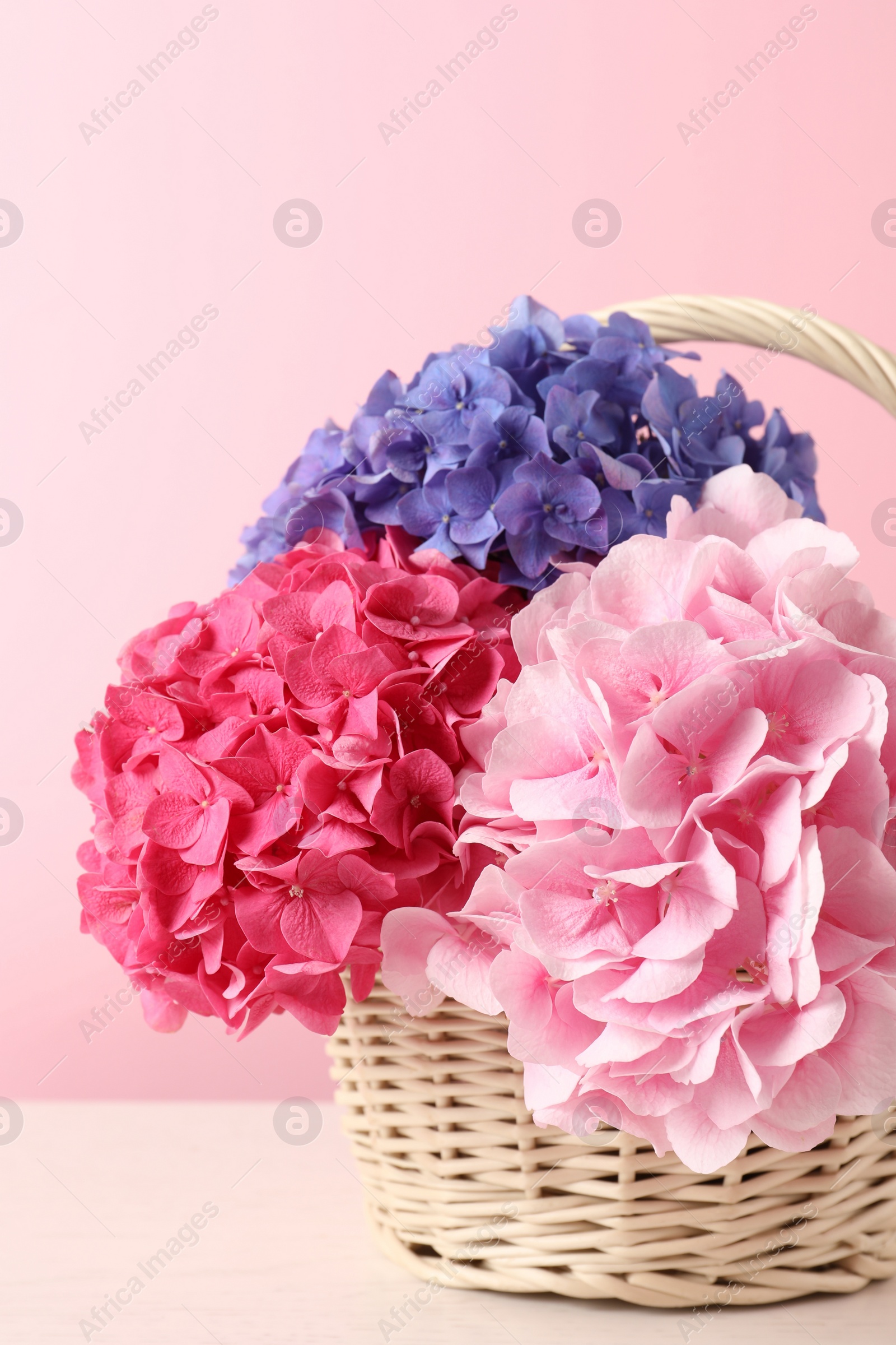 Photo of Bouquet with beautiful hortensia flowers in wicker basket on white wooden table
