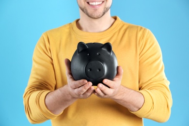 Man with piggy bank on color background, closeup