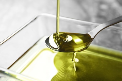 Photo of Pouring hemp oil into spoon over glass bowl, closeup