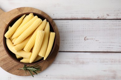 Photo of Tasty fresh yellow baby corns in bowl on white wooden table, top view. Space for text