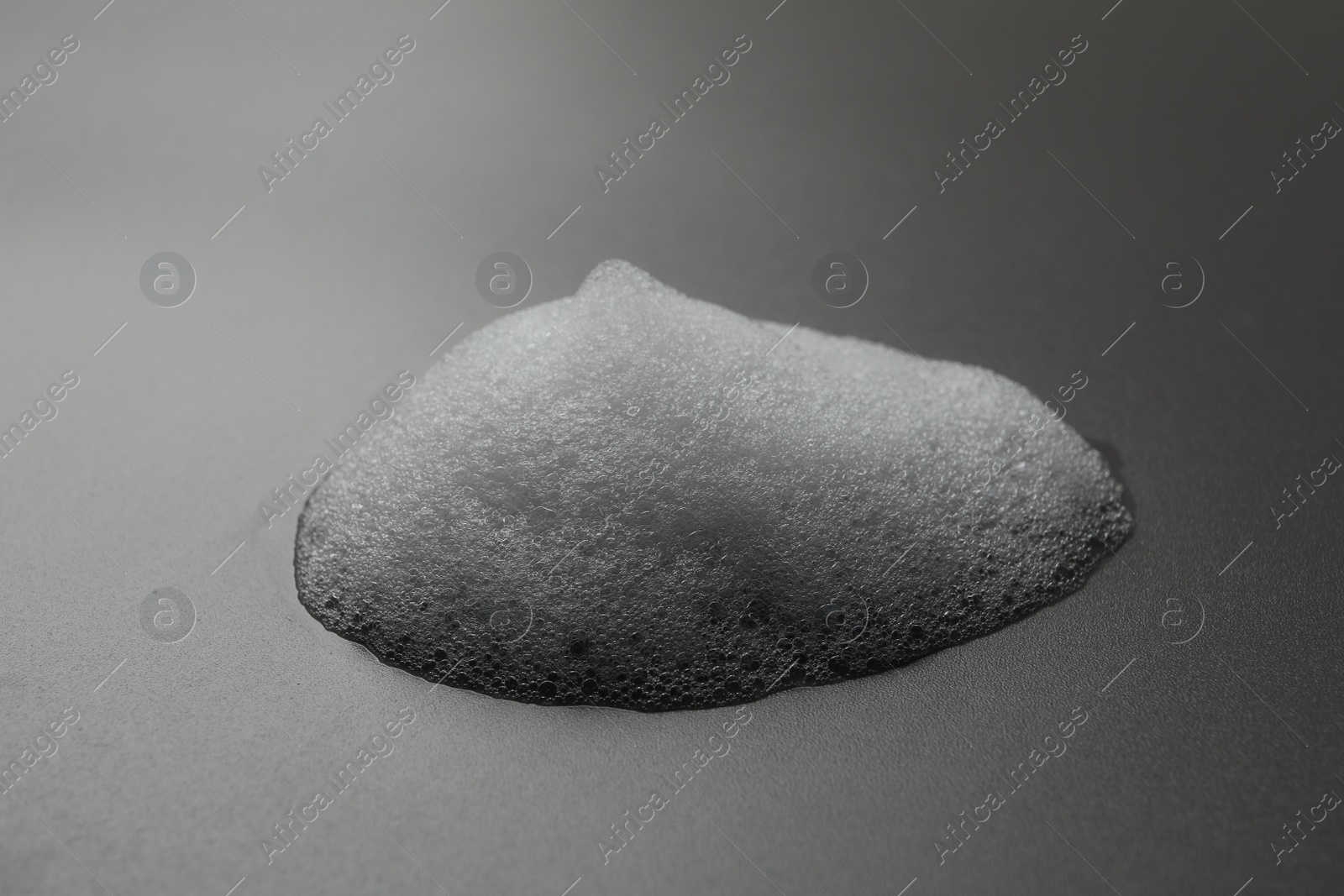 Photo of Drop of fluffy soap foam on grey background