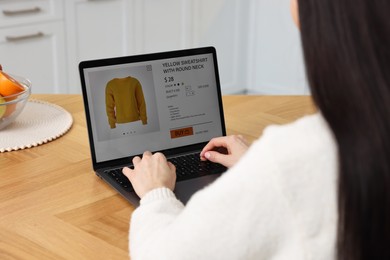 Woman with laptop shopping online at wooden table indoors, closeup