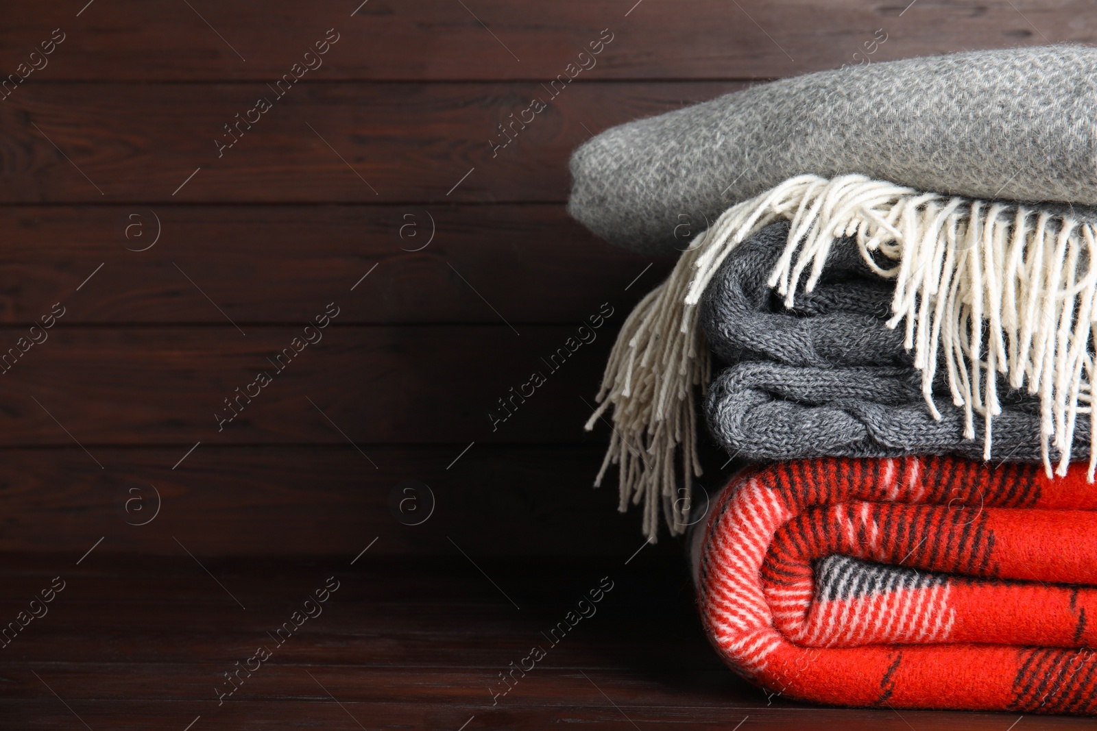 Photo of Stack of soft plaids on brown wooden table, closeup. Space for text