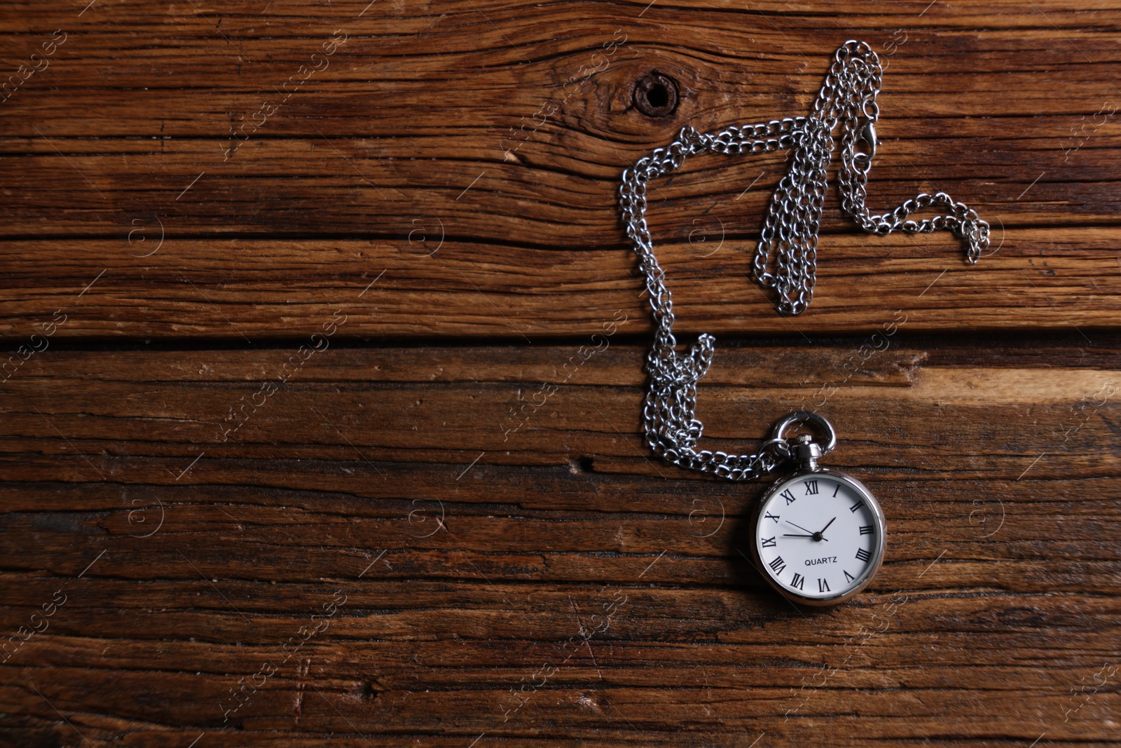 Photo of Silver pocket clock with chain on wooden table, top view. Space for text