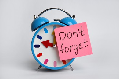 Alarm clock and reminder note with text Don't forget on light grey background