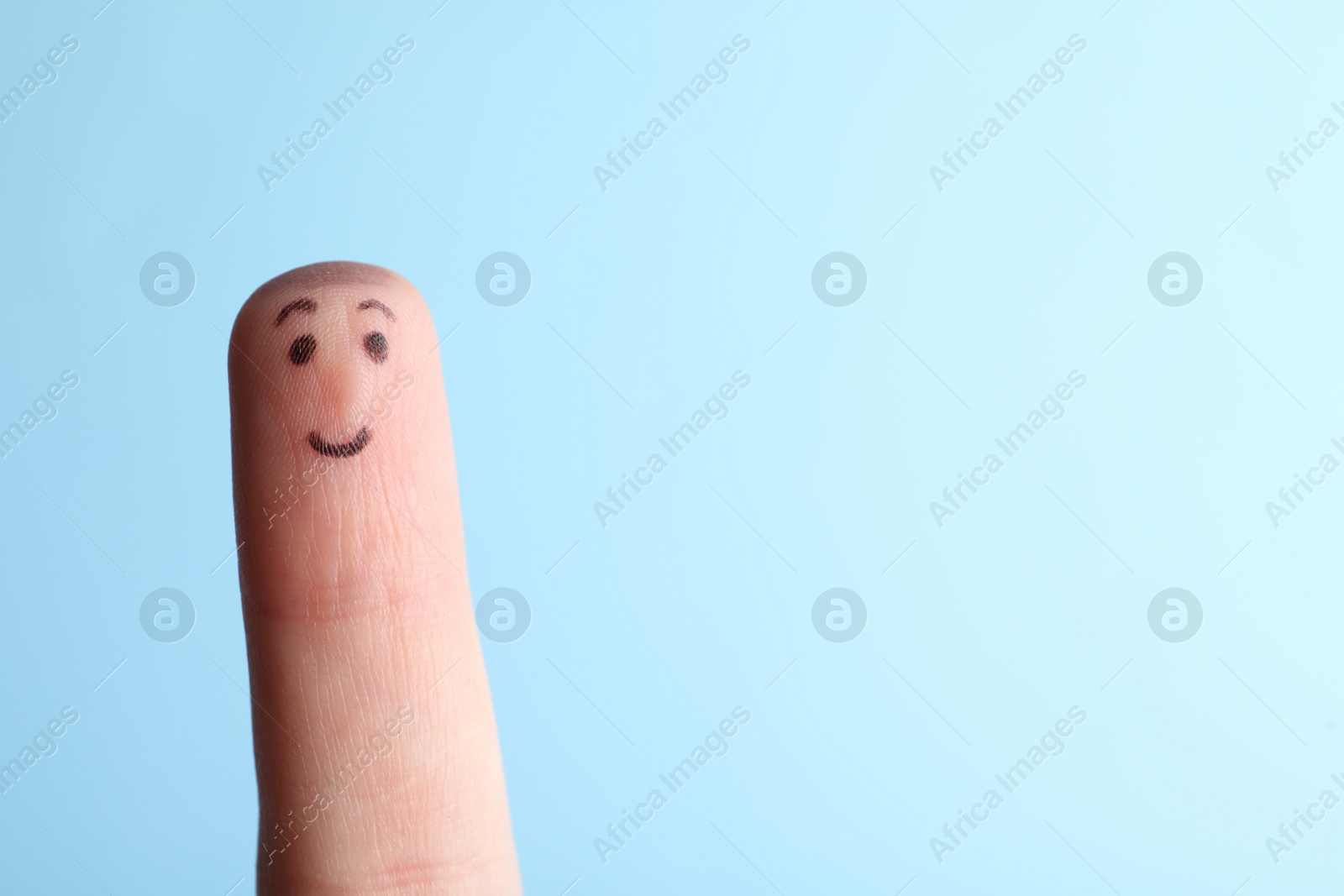 Photo of Finger with drawing of happy face on light blue background. Space for text