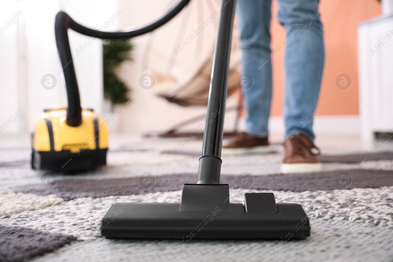 Photo of Young man cleaning carpet with vacuum cleaner at home, closeup