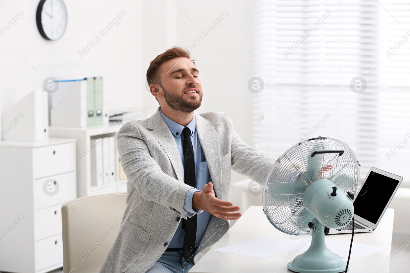 Photo of Man enjoying air flow from fan at workplace