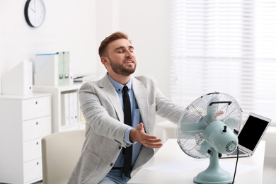 Photo of Man enjoying air flow from fan at workplace