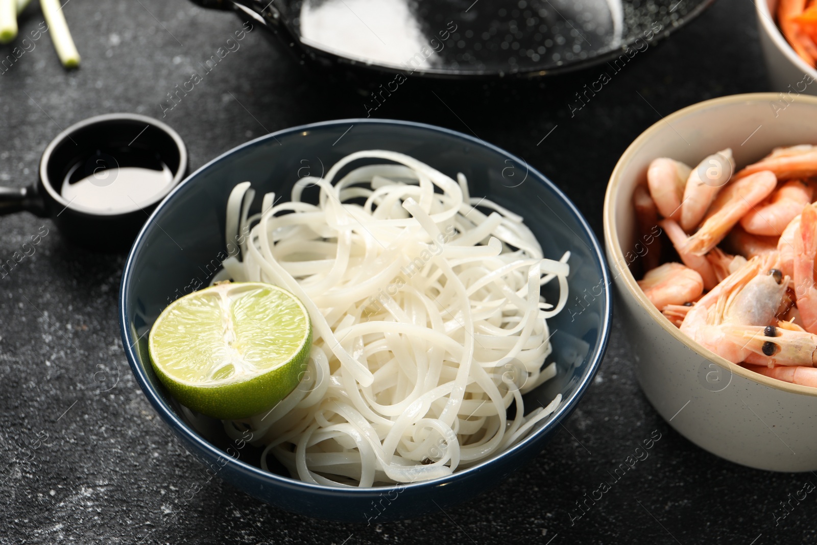 Photo of Noodles, lime and shrimps for cooking wok on grey textured table, closeup