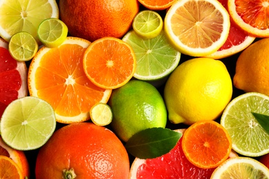 Photo of Sliced and whole citrus fruits with leaves as background, top view