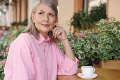 Portrait of beautiful senior woman with cup of coffee at table in outdoor cafe