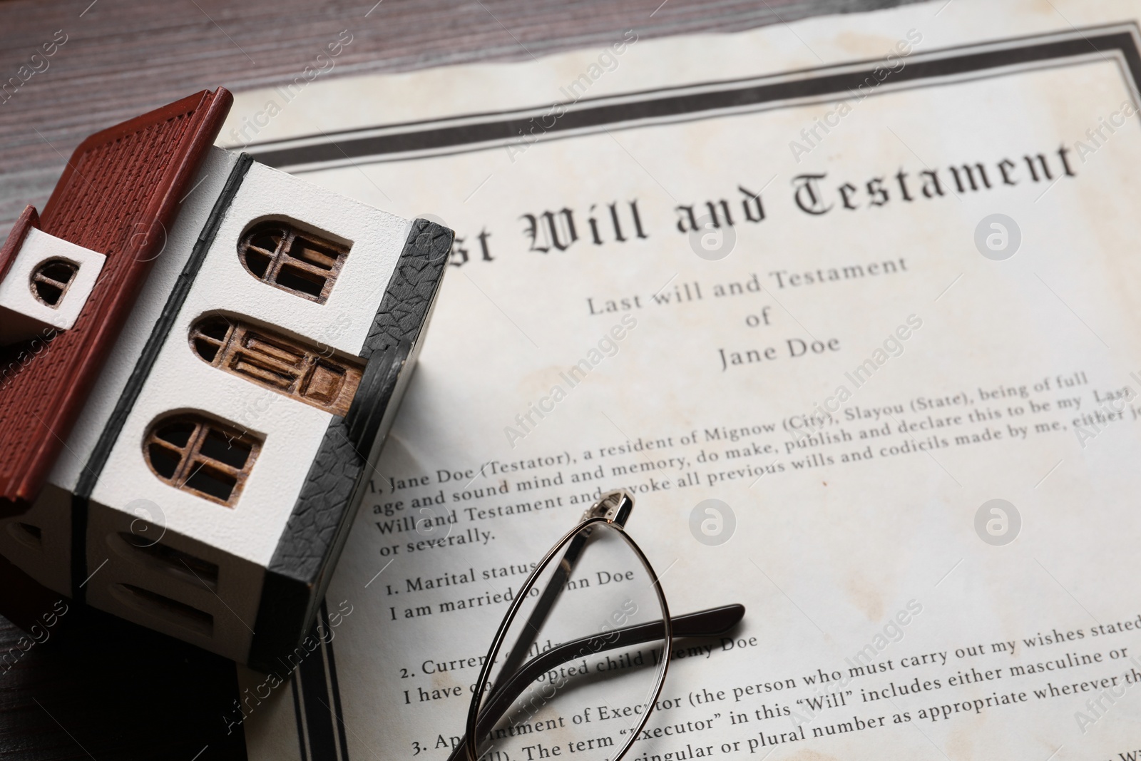 Photo of Last Will and Testament, house model and glasses on wooden table, closeup