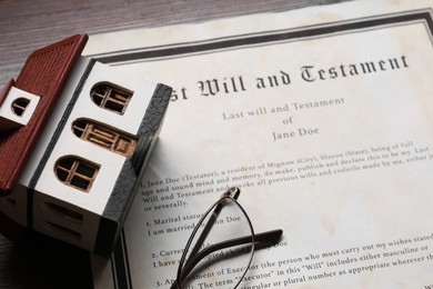 Photo of Last Will and Testament, house model and glasses on wooden table, closeup