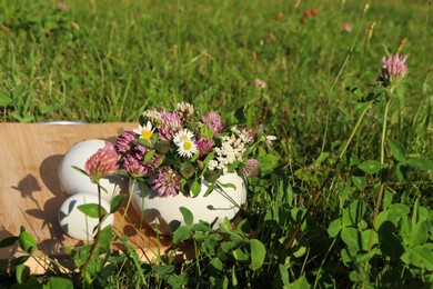 Ceramic mortar with pestle, different wildflowers and herbs on wooden board in meadow