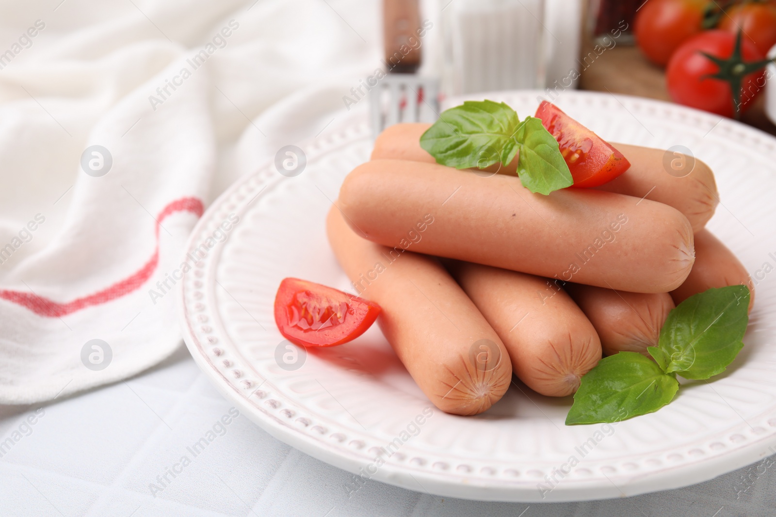 Photo of Delicious boiled sausages, tomatoes and basil on white tiled table, closeup