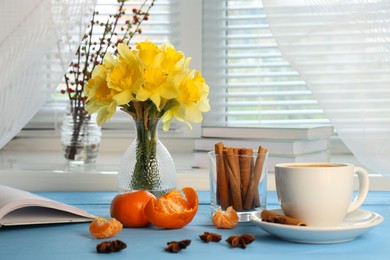 Beautiful yellow daffodils in vase, cup of coffee and tangerines on light blue wooden table