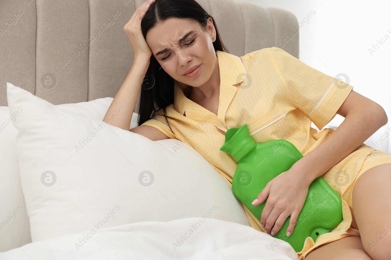 Photo of Woman using hot water bottle to relieve menstrual pain on bed at home