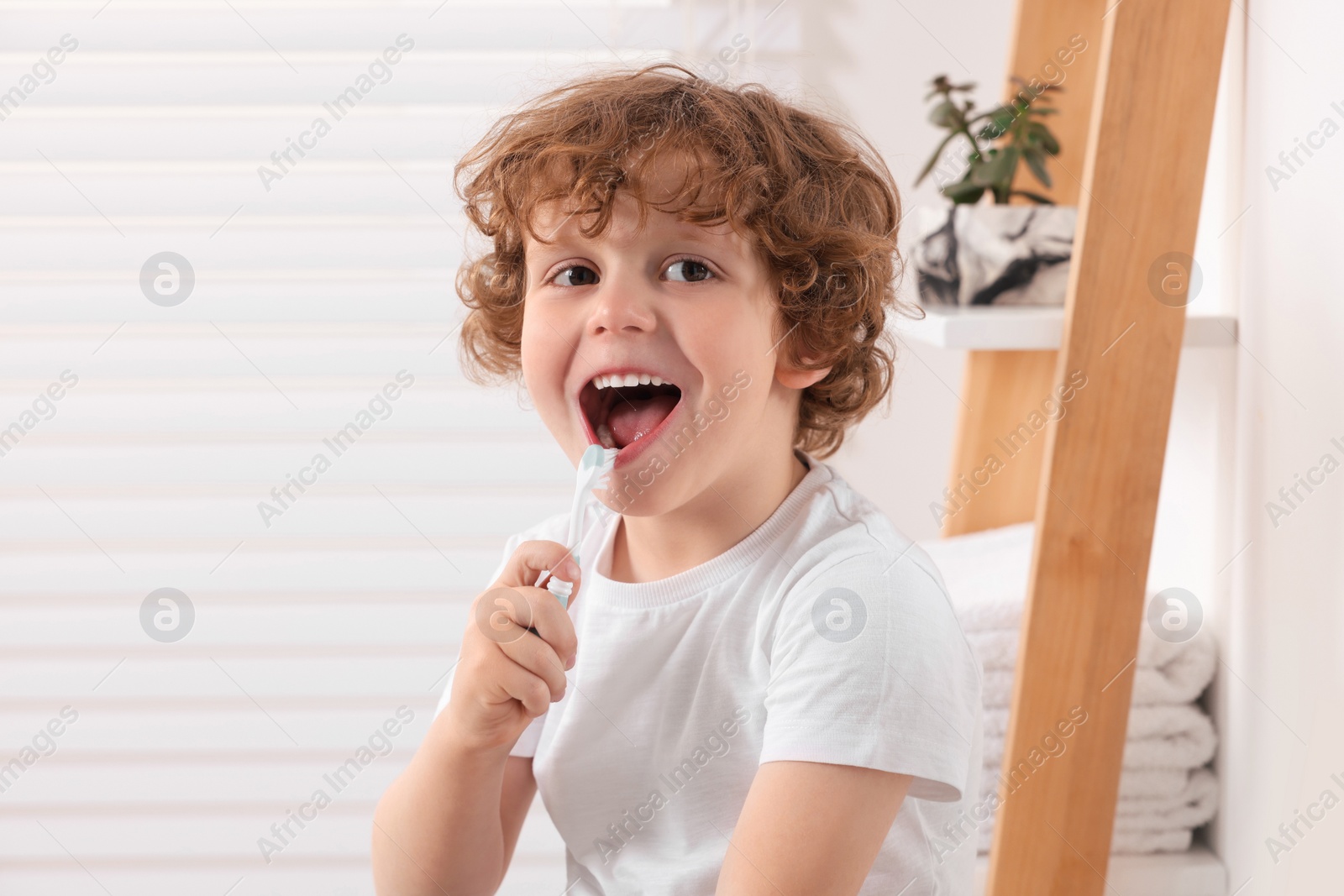 Photo of Cute little boy brushing his teeth with plastic toothbrush in bathroom