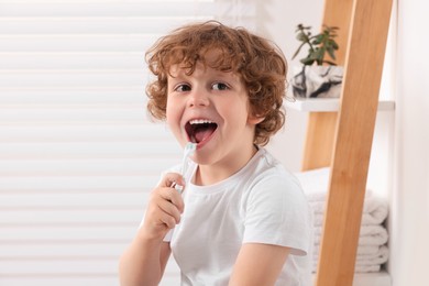 Cute little boy brushing his teeth with plastic toothbrush in bathroom