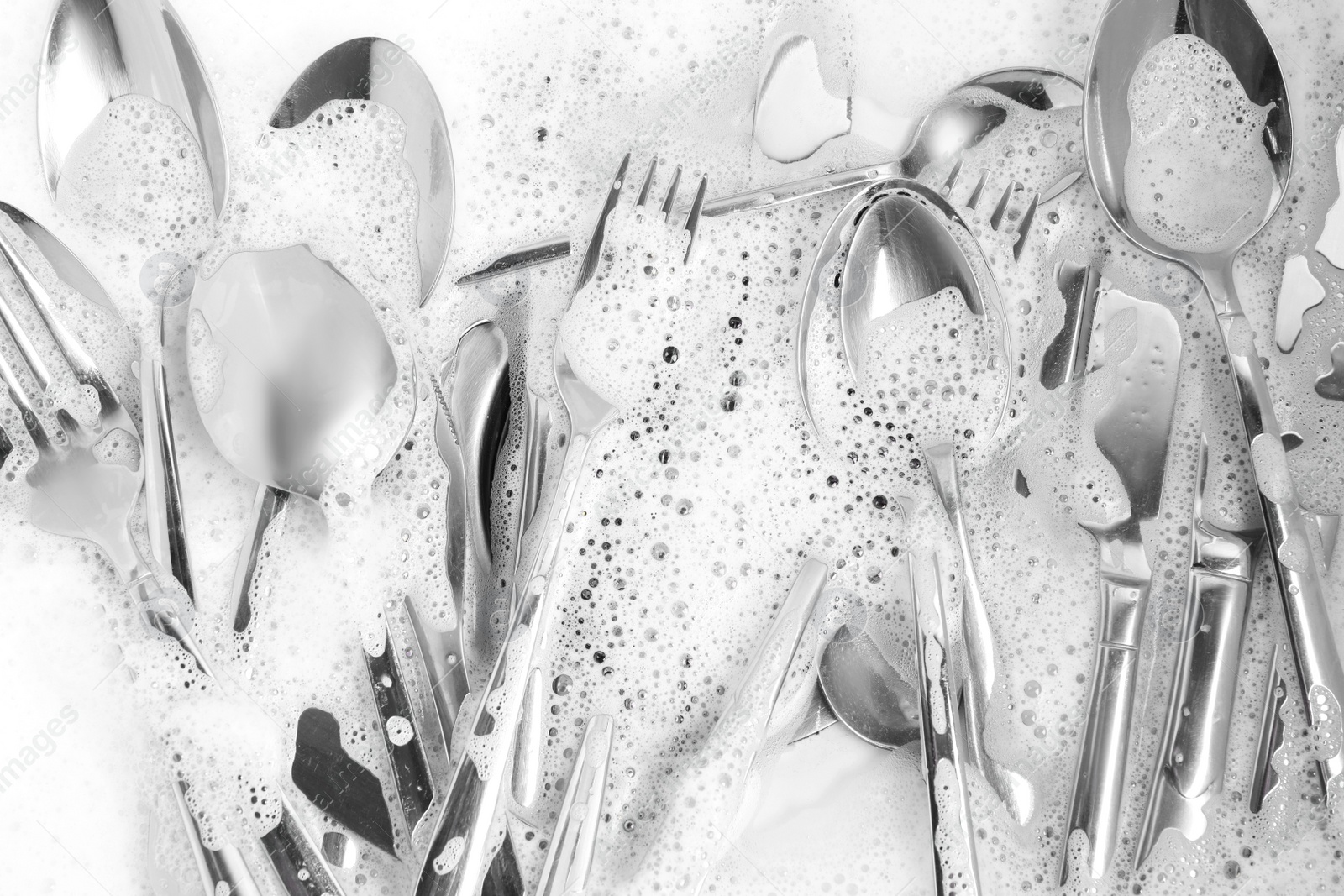 Photo of Washing silver spoons, forks and knives in foam, flat lay