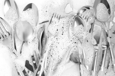 Photo of Washing silver spoons, forks and knives in foam, flat lay