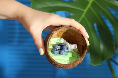 Woman holding coconut shell with tasty smoothie bowl on blurred background, closeup