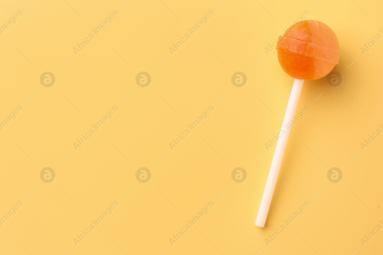 Photo of One tasty lollipop on yellow background, top view. Space for text