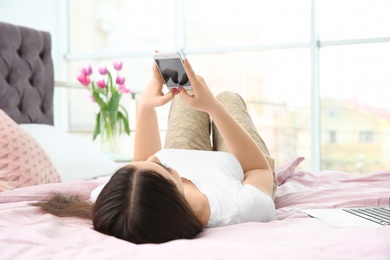 Beautiful young woman taking selfie on bed at home