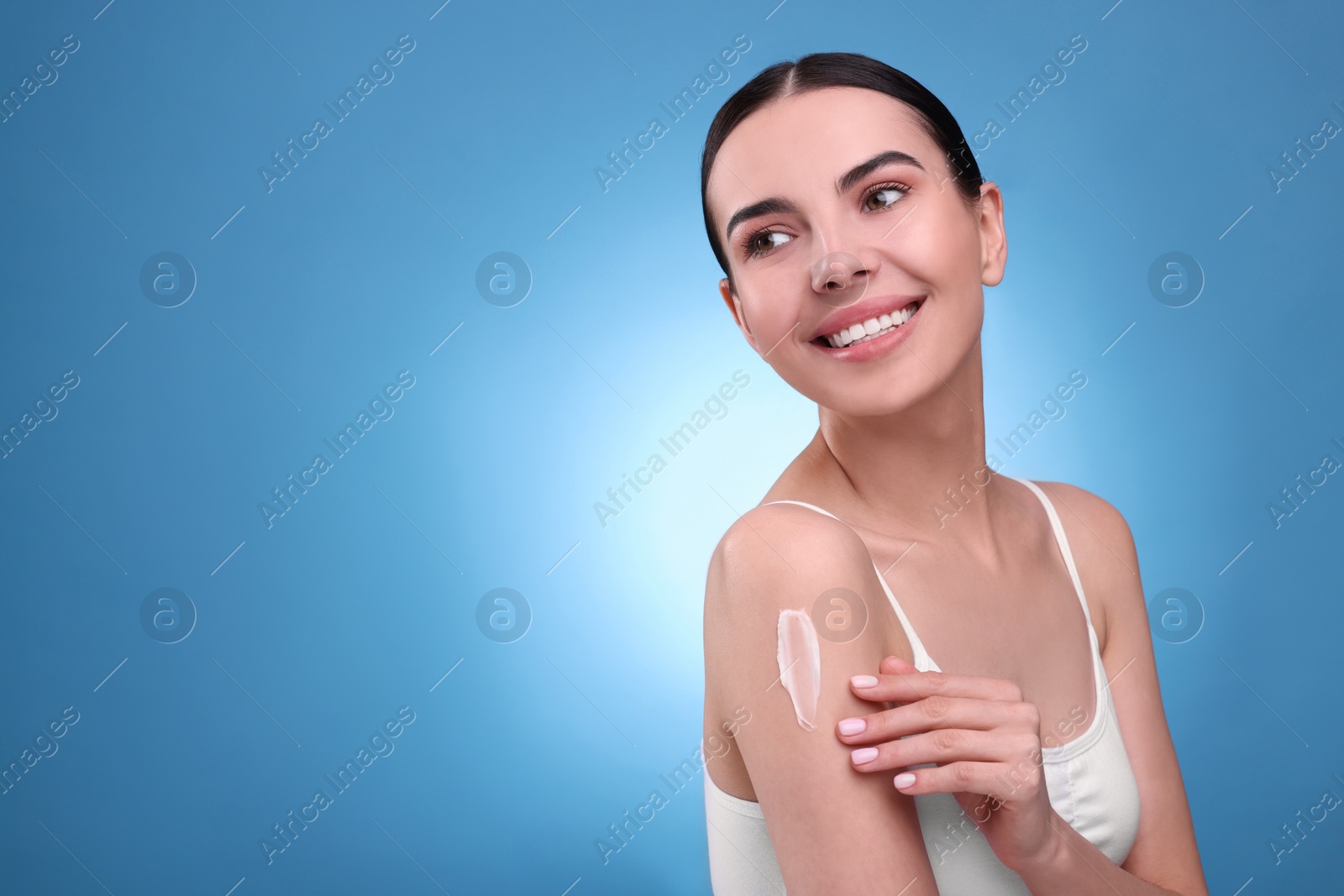 Photo of Beautiful woman with smear of body cream on her shoulder against light blue background, space for text