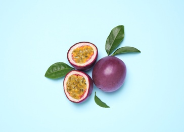 Fresh ripe passion fruits (maracuyas) with green leaves on light blue background, flat lay