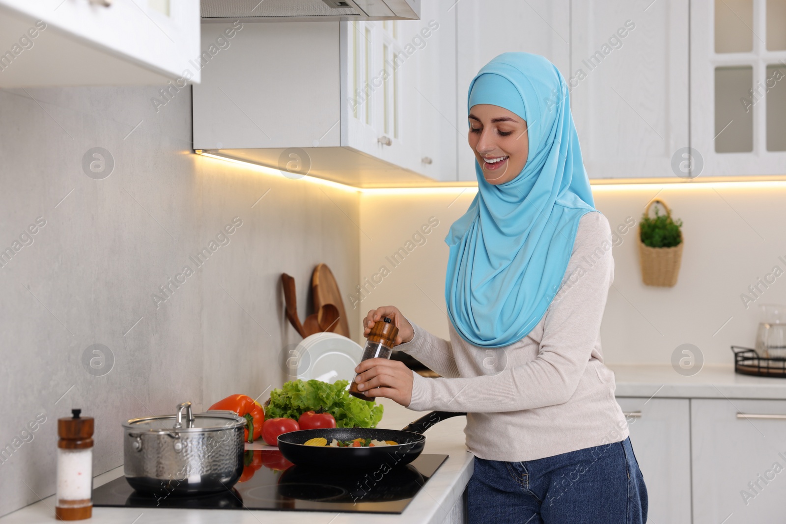 Photo of Muslim woman cooking dish in frying pan on cooktop indoors