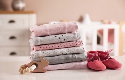 Photo of Stack of clean girl's clothes, booties and toy on table indoors