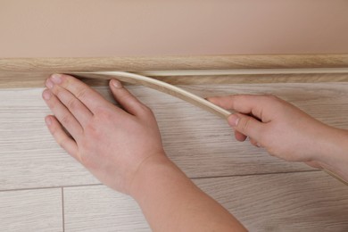 Photo of Man installing plinth on laminated floor in room, closeup