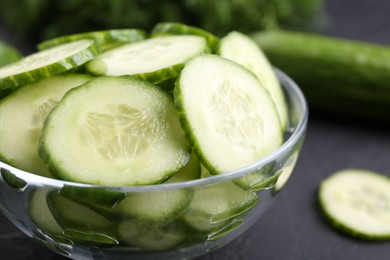 Photo of Cut cucumber in glass bowl on dark gray table, closeup